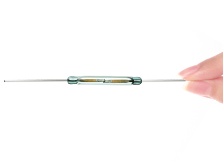 A hand holding a small glass Standex Detect reed switch with metal leads extending from both ends, against a white background. by Standex Detect