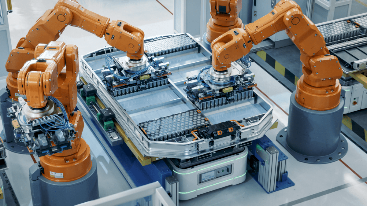Four orange robotic arms assemble a large battery pack on an automated production line in a modern, clean factory setting, precisely managing inrush current as detailed machinery and neatly organized parts ensure seamless operation. by Standex Detect