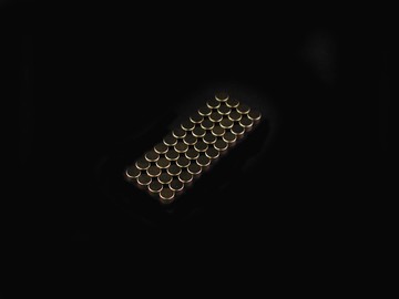 A rectangular grid of small, round, metallic objects—possibly sensors to measure speed—is arranged neatly in rows on a black background. by Standex Detect