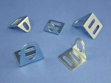 Five metal brackets with oval and rectangular holes, designed to accommodate sensors to measure speed, are arranged on a blue surface. by Standex Detect