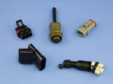 Five assorted electrical connectors are arranged on a light blue background. The connectors vary in size, shape, and color, with some featuring multiple pins or circular designs often used for sensors to measure speed. by Standex Detect