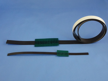 Three black plastic strips, one coiled, with green textured connectors on a blue background. The top strip is coiled with a white edge; the other two strips are laid flat with connectors attached—these versatile strips can be used with sensors to measure speed in various applications. by Standex Detect
