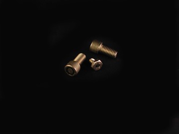 Two metallic bolts and one hex nut are arranged on a plain black background, with soft lighting highlighting their surfaces—evoking the precision engineering often required for sensors to measure speed. by Standex Detect