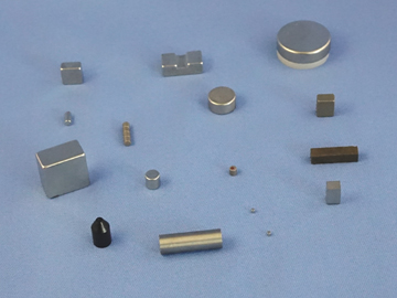 A collection of various small industrial magnets of different shapes, sizes, and colors—including cylinders, cubes, blocks, and a small black cone—scattered across a flat, light blue surface. These versatile magnets can be integrated with sensors to measure speed in precision-driven industrial applications. by Standex Detect